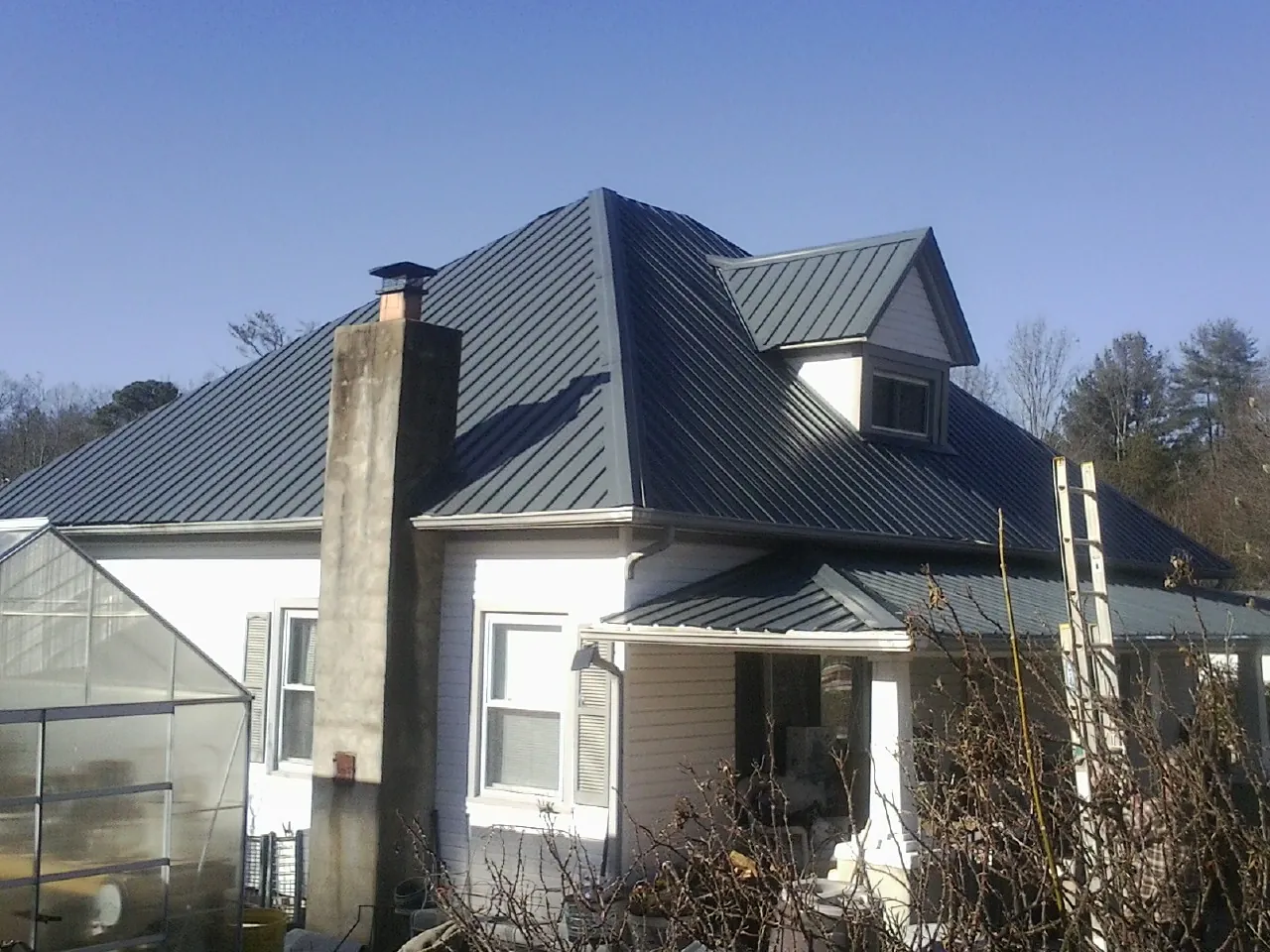 Dark blue standing seam metal roof on a white farmhouse with dormer — Slate & Tile Roof Repair by Roofing Brothers in Plover