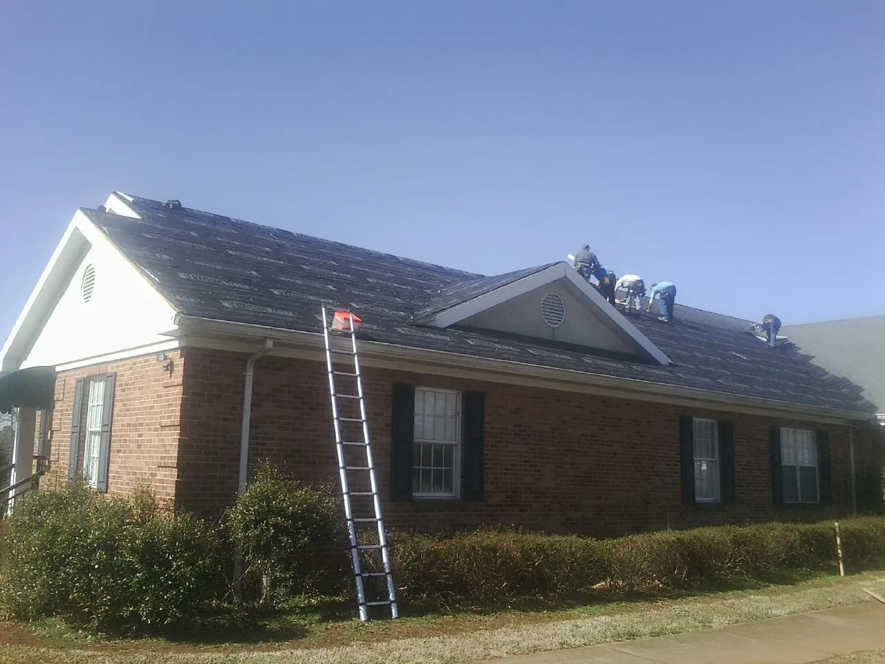 Crew tearing shingles off a brick ranch roof with a ladder set — Emergency Roof Repair work by our crew in Plover
