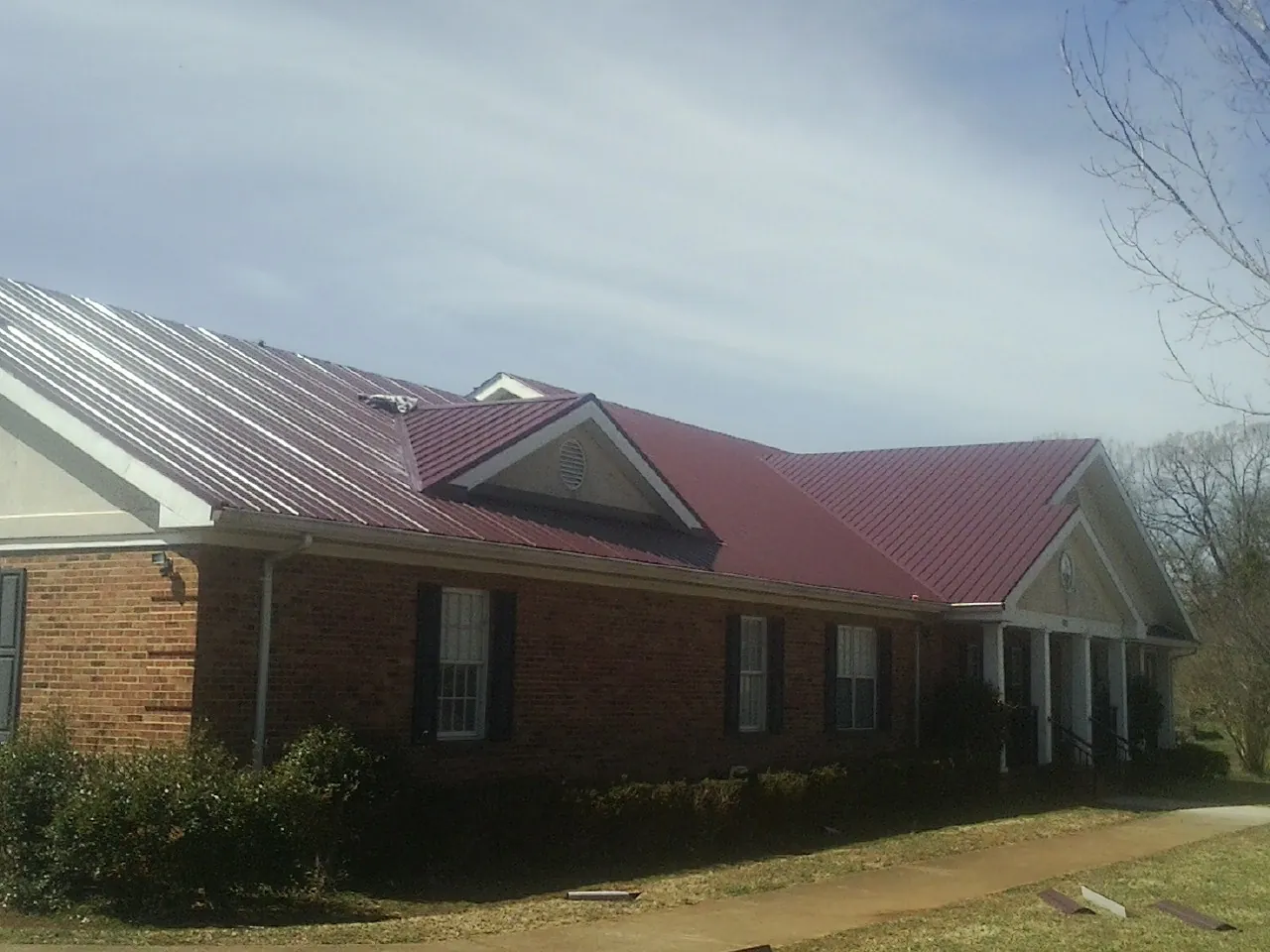 Red metal roof with gabled entries on a long brick building, from a Hail Damage Roof Repair job in Plover