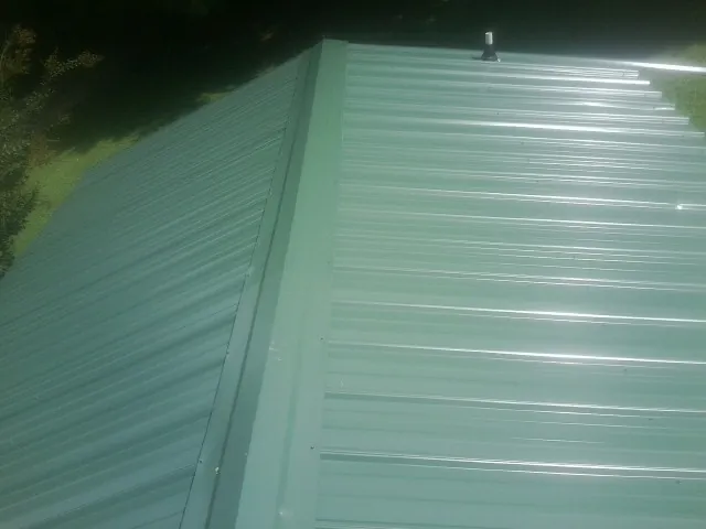 New green metal panels meeting at the ridge of a roof — Flat Roof Repair work by our crew in Plover