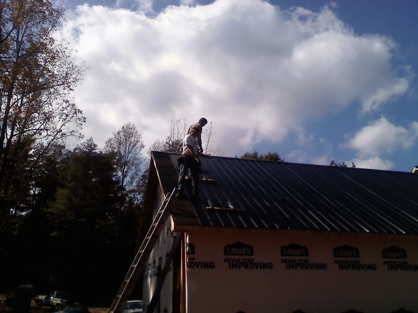 Roofer fastening dark metal panels high against a cloudy sky, from a Roof Inspection job in Plover