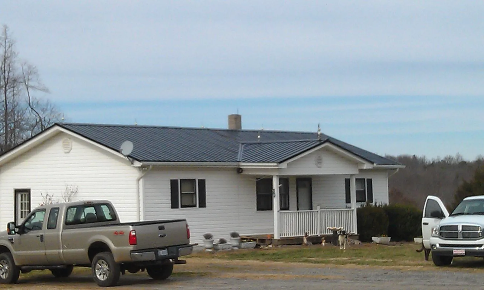 Finished dark metal roof on a white ranch home with work trucks parked in Plover