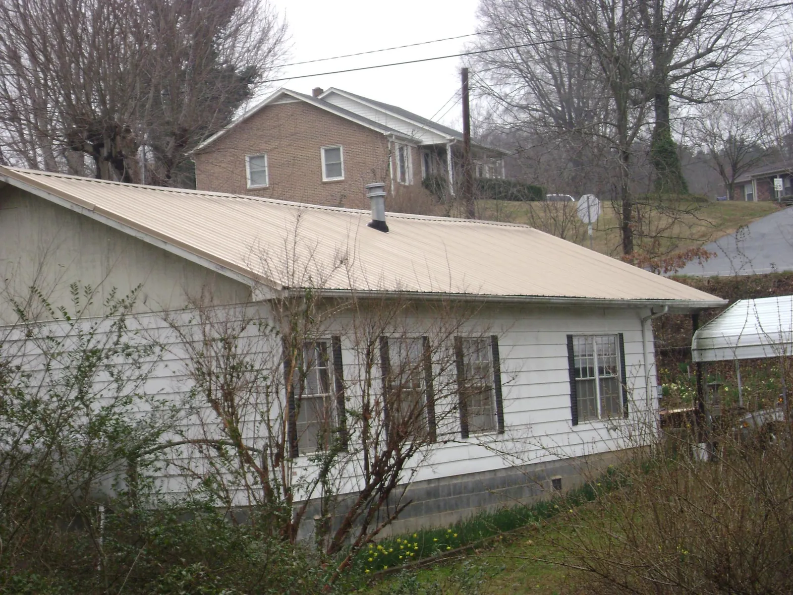 Tan metal roof on a white sided house set into a hillside — Commercial Roofing by Roofing Brothers in Plover